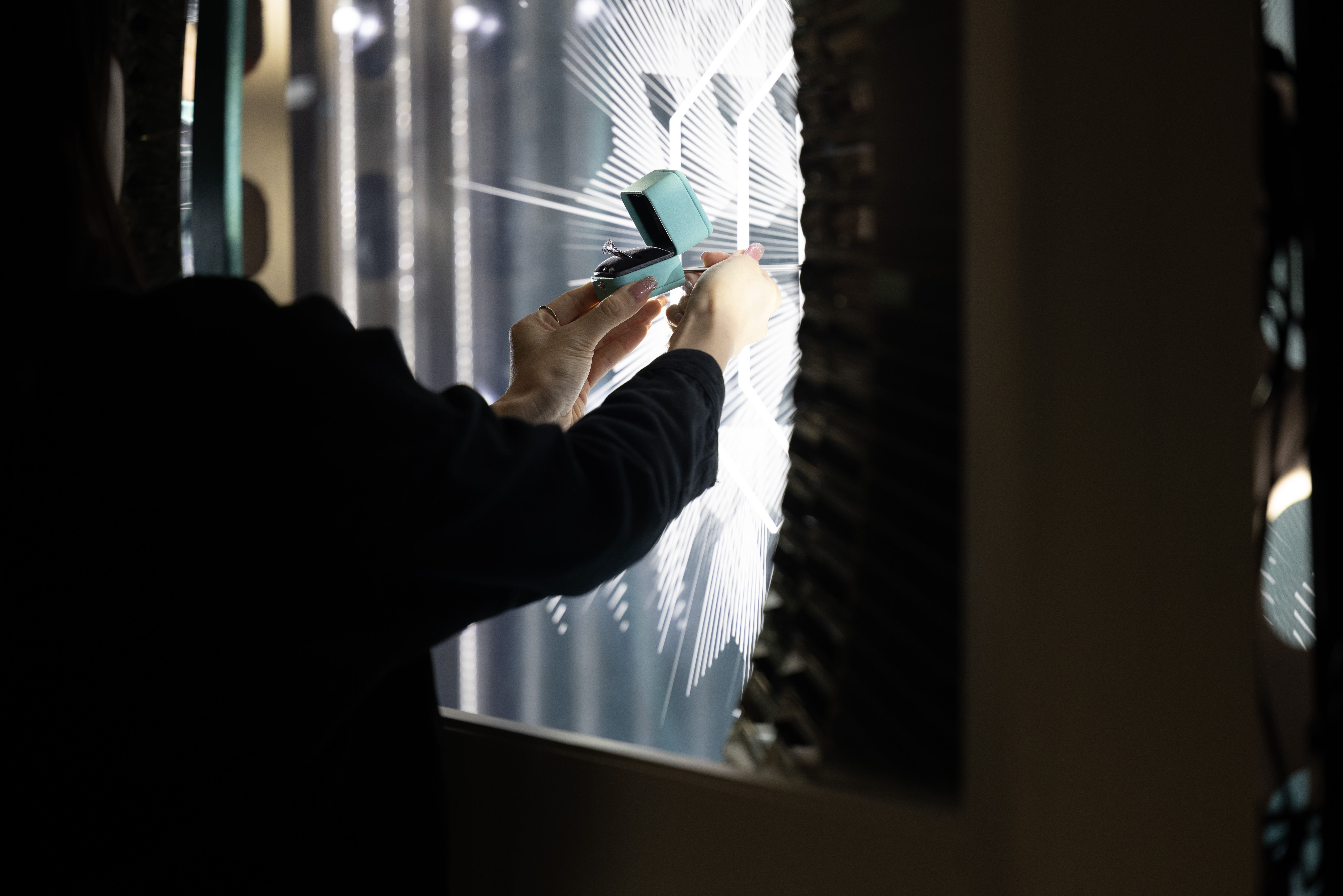 Artisan placing a sparkling Tiffany ring in its box in front of a backlit geometric window display, showcasing intricate light patterns