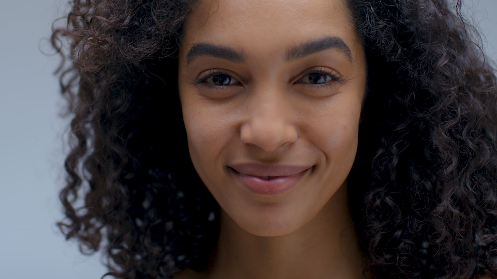 Close-up of a woman with curly hair and radiant skin, representing the beauty and wellness focus of Nutrafol x Sephora Skin campaign.