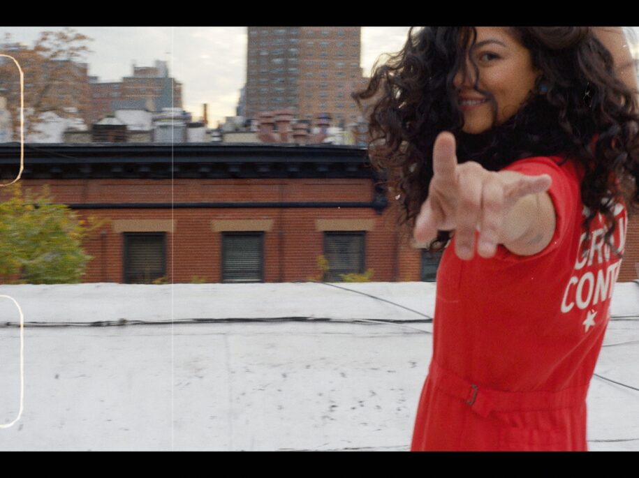 SoulCycle instructor Soureya in a striking red outfit reaches out against a cityscape, her playful gesture inviting viewers into the engaging world of SoulCycle, as seen in the brand's inspiring docufilm