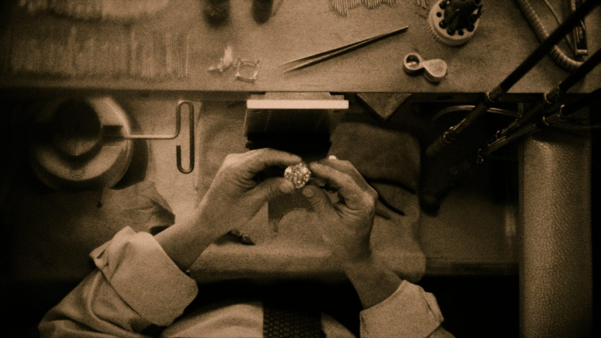 Sepia-toned photo of a Tiffany & Co. jeweler meticulously inspecting a diamond ring, highlighting the intricate craftsmanship in a workshop setting.