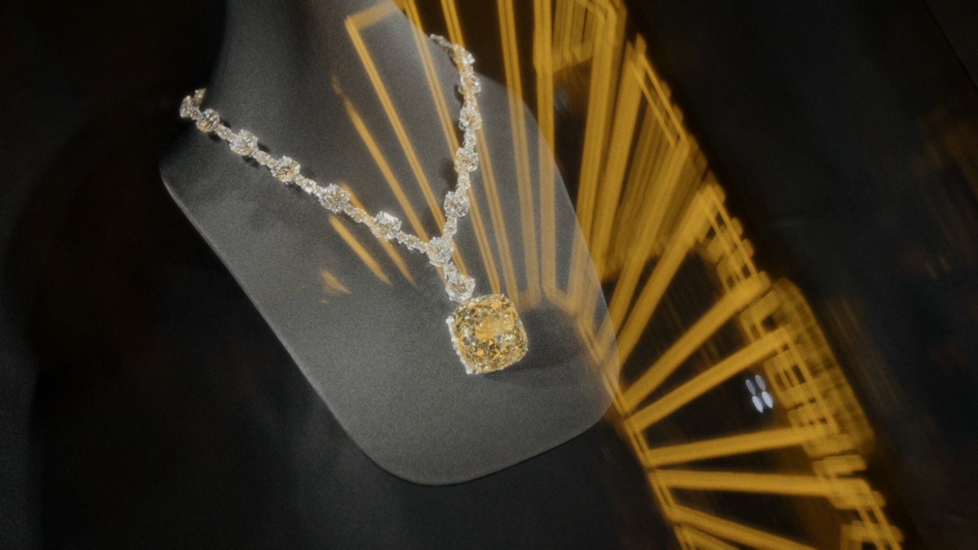 Stunning display of a Tiffany & Co. diamond necklace with a large yellow central diamond, elegantly draped on a mannequin with a radiant reflection of light creating a dynamic backdrop.