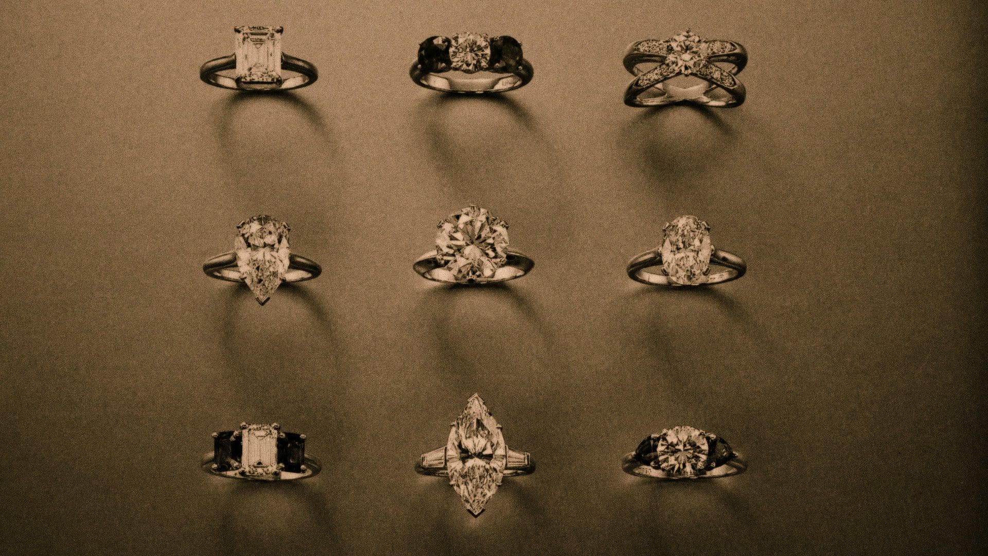 Sepia-toned image displaying a selection of nine Tiffany & Co. engagement rings, each featuring the revolutionary Tiffany setting that elevated diamond jewelry design, against a dark backdrop.