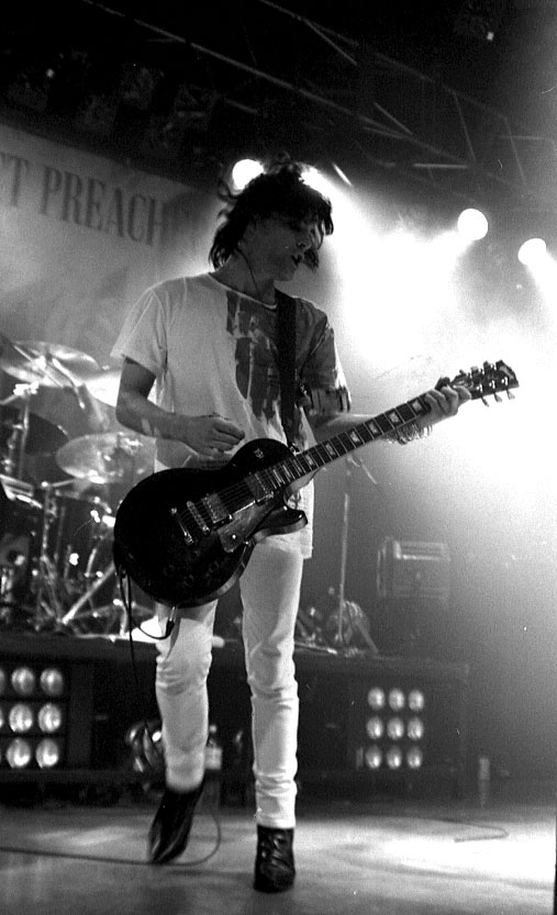 Richey Edwards performing live with Manic Street Preachers, holding a guitar and wearing a white t-shirt