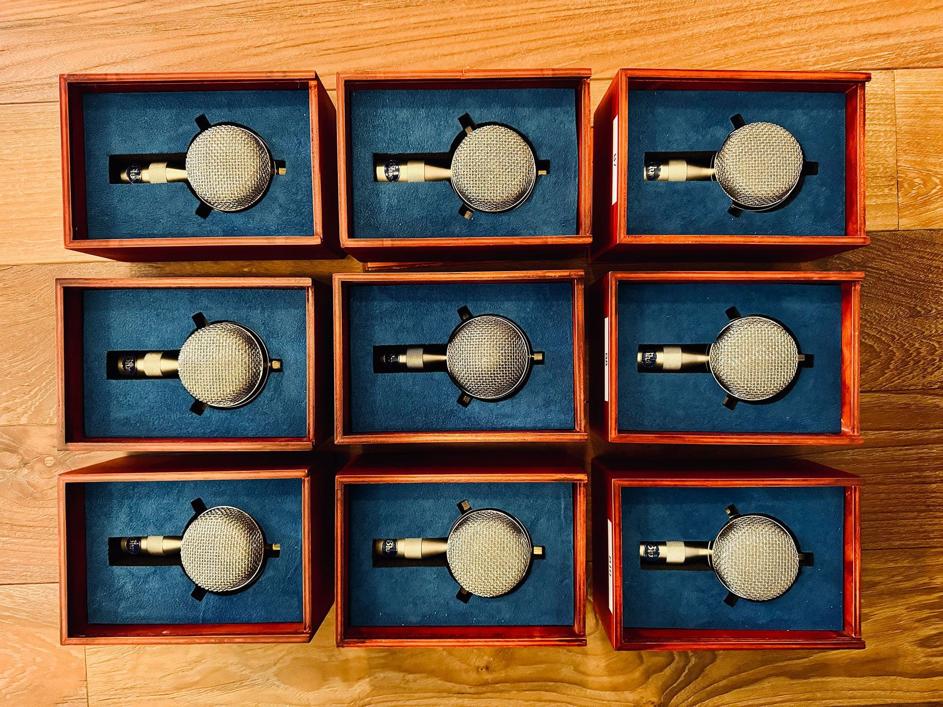 Array of Blue Bottle microphone capsules in wooden boxes with blue velvet lining, displayed on a wooden surface